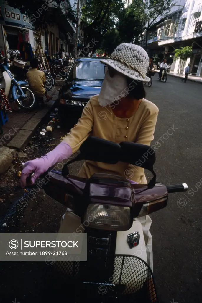 VIETNAM, Ho Chi Minh City. Woman on moped wearing a scarf over her nose and mouth to protect against the smog.. 