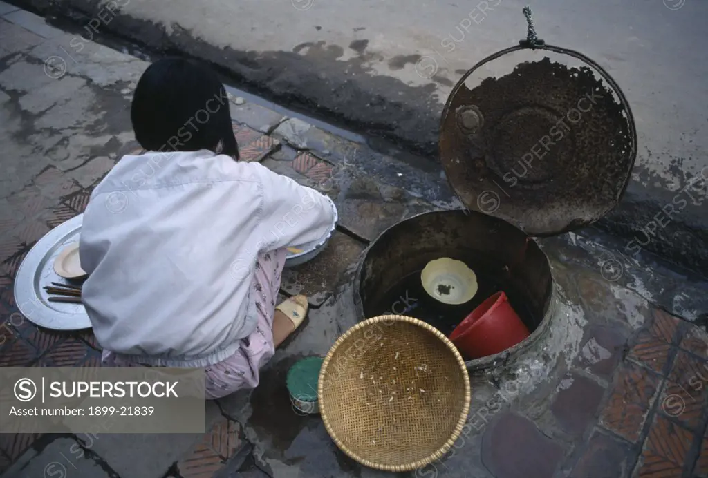 VIETNAM North Hanoi. Girl washing pots in a communal water well in the pavement beside a drain..  