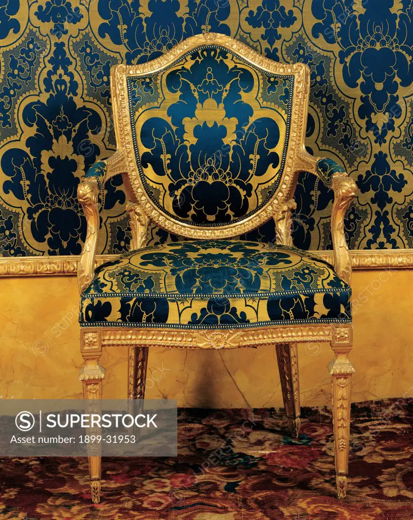 Armchair, by Toussaint Carlo, 1794, 18th Century, wood carved,gilded and partially painted, padded seat, back and sides covered with damask silk. Italy, Tuscany, Florence, Palazzo Pitti, Winter Quarters, King's Bedroom. Whole artwork. Armchair chair seat upholstery silk damask damask fabric: tissue colors gold blue embroidery decoration fittings design piece of furniture furniture shield-shaped backrest pyramidal legs classical motifs Greek-sty.