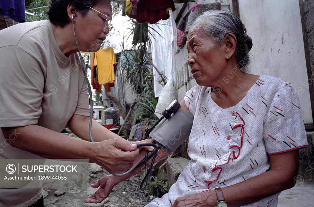 HEALTHCARE, PHILIPPINES. Manila. Payatas. Voluntary health worker checking the blood pressure of elderly lady. . 