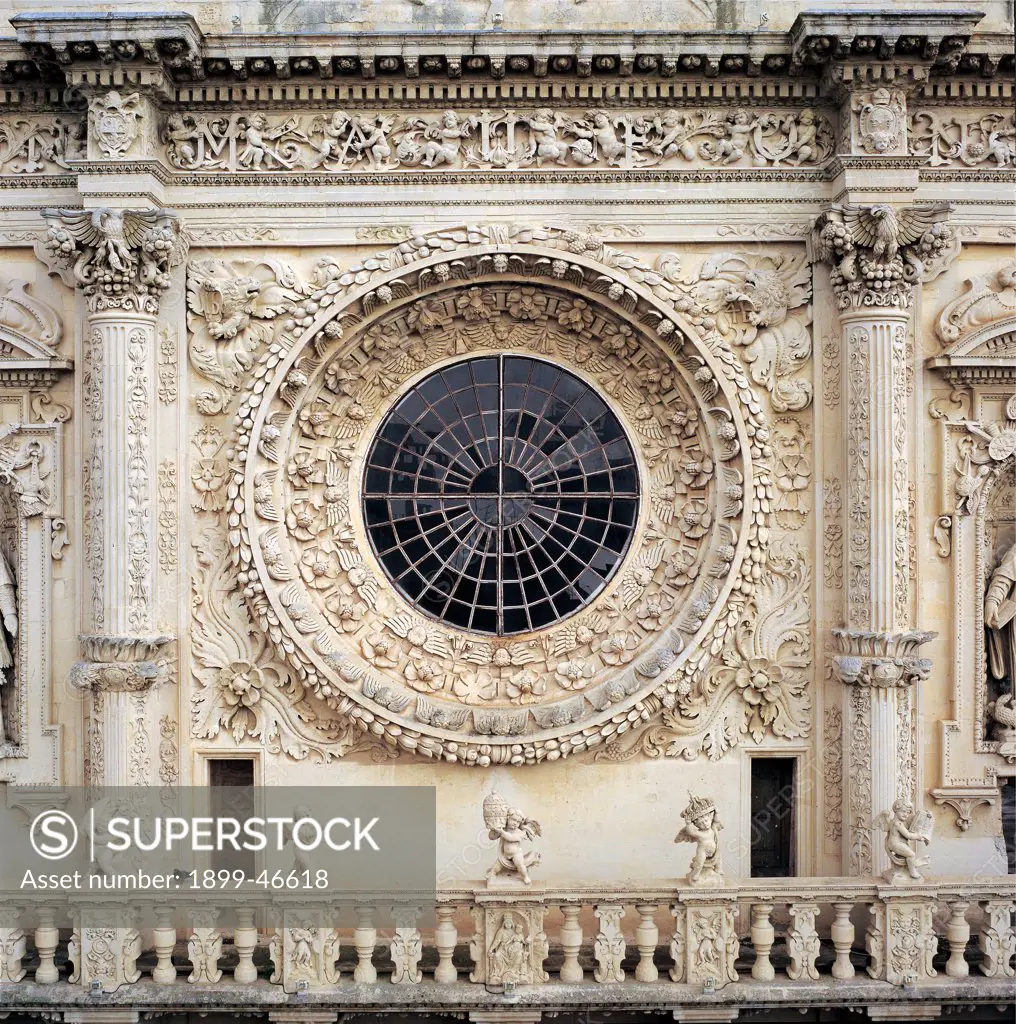Church of Santa Croce in Lecce, by Zimbalo Francesco Antonio, Riccardi Gabriele, 1549 - 1695, 17th Century, Lecce stone. Italy: Puglia: Lecce: Lecce: Santa Croce Church. Detail. Exterior Church of Santa Croce facade upper tier/order window rose-window carved cornices bas-relief columns capital grotesques festoons fruit pelican flowers leaves angels cherubs garland