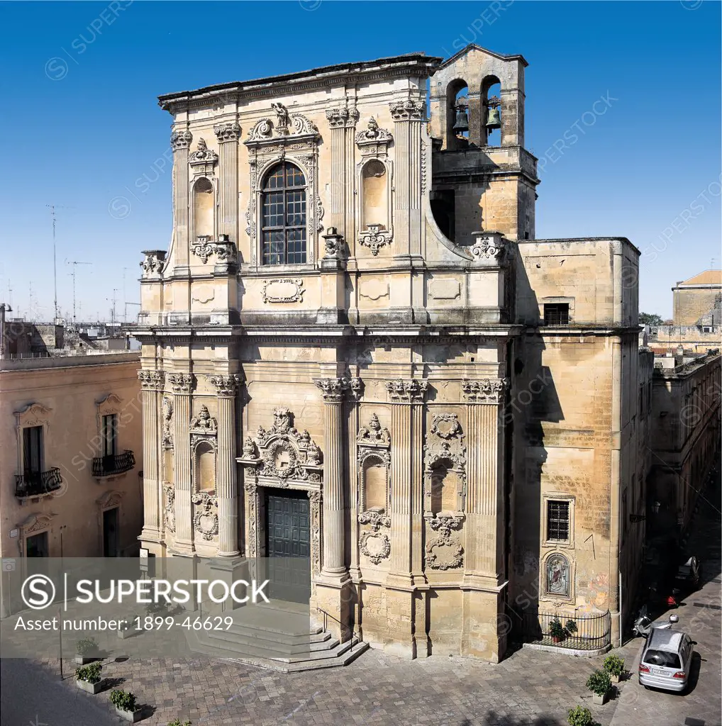 Santa Chiara Church, Lecce, by Cino Giuseppe, 1687, 17th Century, Lecce stone. Italy: Puglia: Lecce: Lecce: Gesu Church. Whole artwork. Santa Chiara church foreshortened view facade superimposed tiers doorway carved piers pediment carved mixtilinear tympanum/gable crest/coat of arms Corinthian grooved columns pilaster-strips Corinthian capital niches garlands medallions cornice string-course window cornice belfry bells