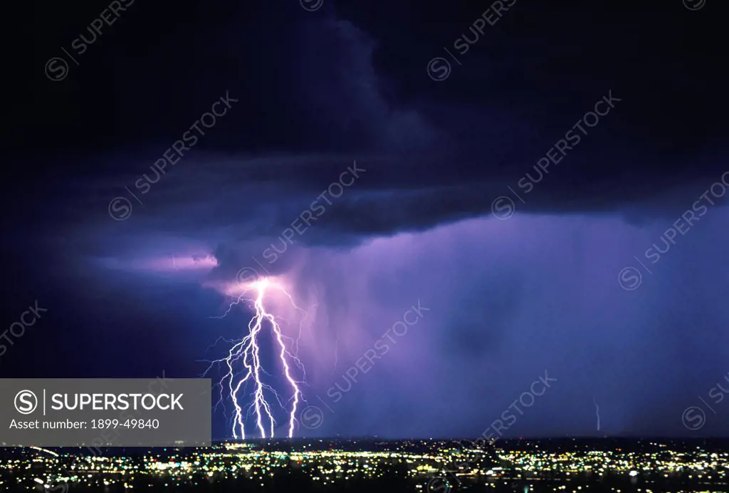 Five cloud-to-ground lightning strikes on leading edge of rain curtain sweeping over city at night.  Tucson, Arizona, USA.