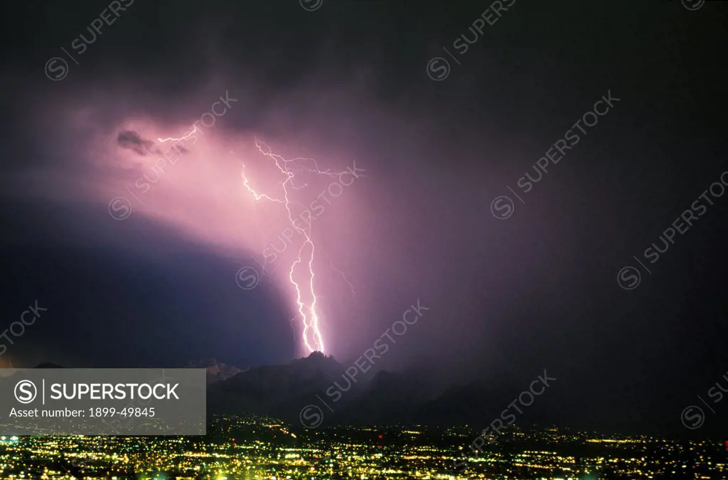 Two powerful cloud-to-ground lightning strikes in the west end of the Santa Catalina Mountains with city lights in foreground.  Tucson, Arizona, USA.