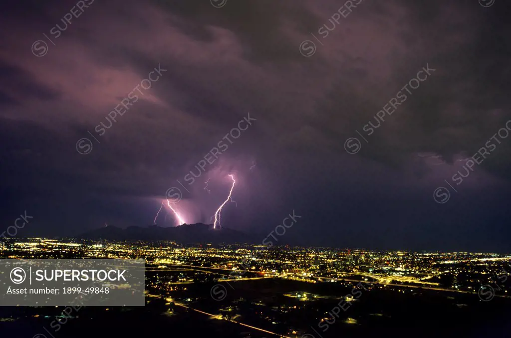 Nighttime cityscape with storm clouds and cloud-to-ground lightning over the Santa Catalina Mountains.  Tucson, Arizona, USA.