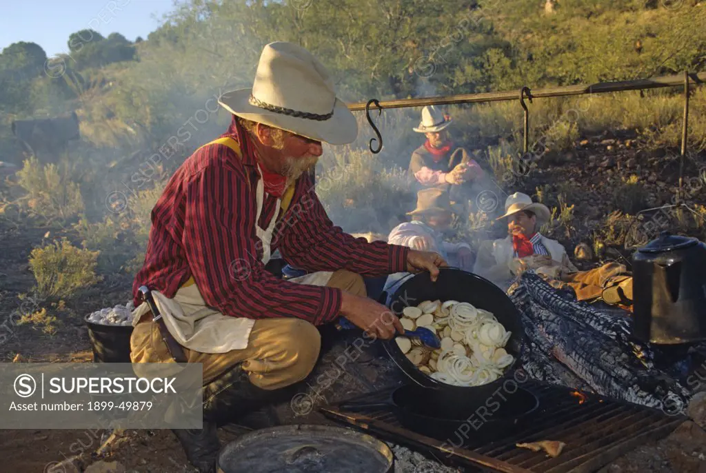 Chuckwagon cook Mike Ryan prepares breakfast (frying potatoes and onions) at cowboy camp. Cattle drive organized by Dan Bates, Cobra Ranch, Agro Land and Cattle Company. Galiuro Mountains, Arizona, USA. October 1993  In background: rear, Thomas Hirt (a Tucson hatmaker); right, Dan Bates; left front, John Cleator, Jr.