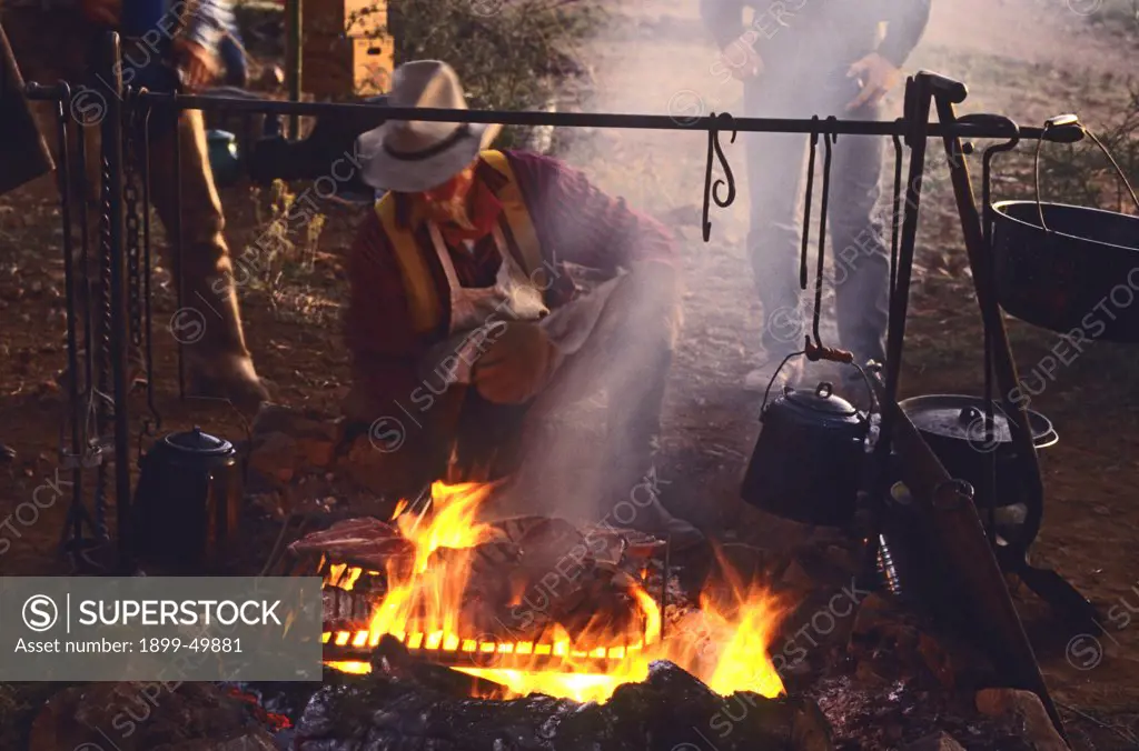 Chuckwagon cook Mike Ryan grills steaks for dinner over an open fire at cowboy camp. Cattle drive organized by Dan Bates, Cobra Ranch, Agro Land and Cattle Company. Galiuro Mountains, Arizona, USA. October 1993.