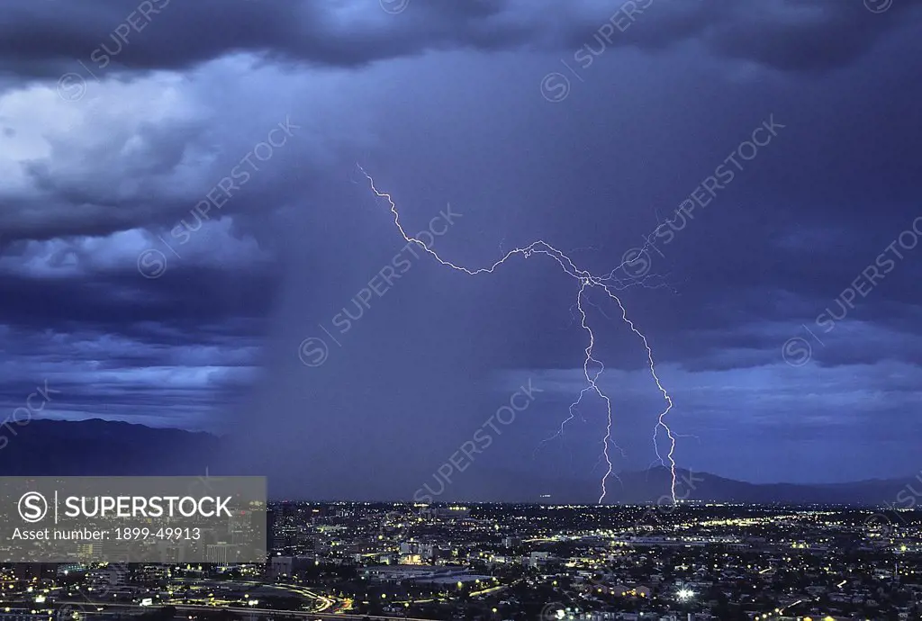 Twilight view, just after sunset, of forked ground discharge lightning as it leaps ahead of a rain shaft over city.  Tucson, Arizona, USA.