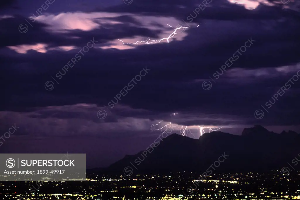 Stormy sky at twilight, shortly after sunset, with air discharge lightning high in the clouds and cloud-to-ground discharges over the Santa Catalina Mountains.  Tucson, Arizona, USA.