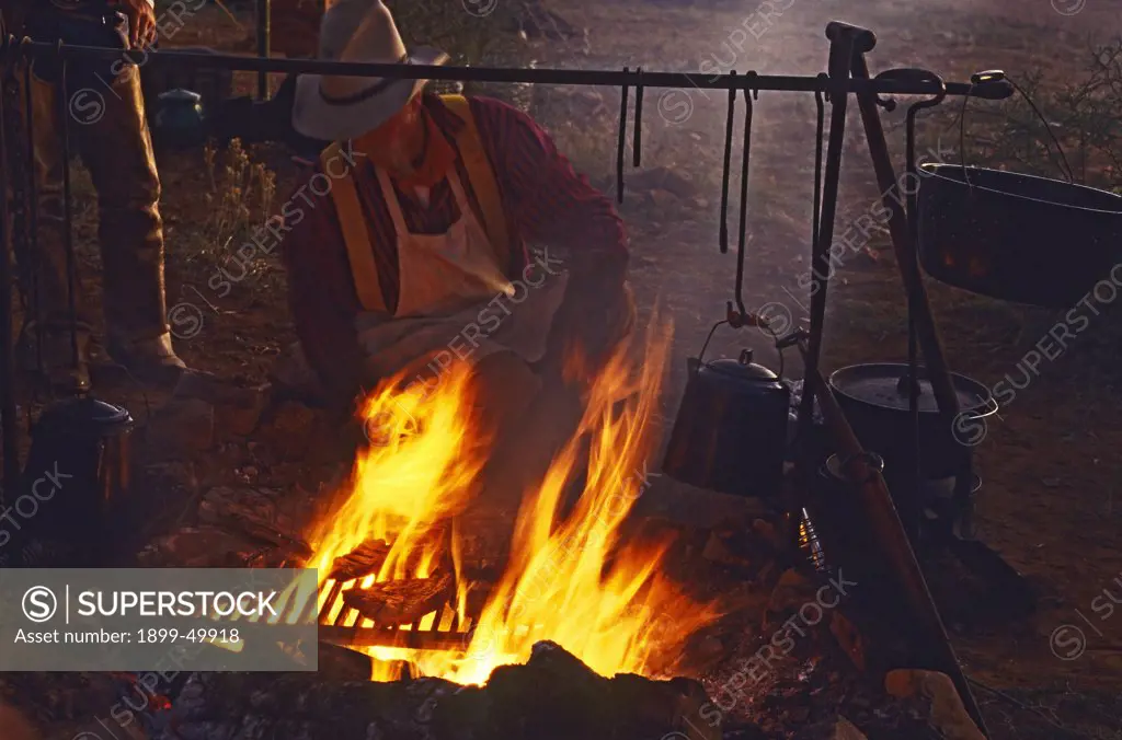 Chuckwagon cook Mike Ryan grills steaks for dinner over an open fire at cowboy camp. October 1993. Cattle drive organized by Dan Bates, Cobra Ranch, Agro Land and Cattle Company. Galiuro Mountains, Arizona, USA. (October 1993).  (Restricted use; contact Thomas Wiewandt for details.)