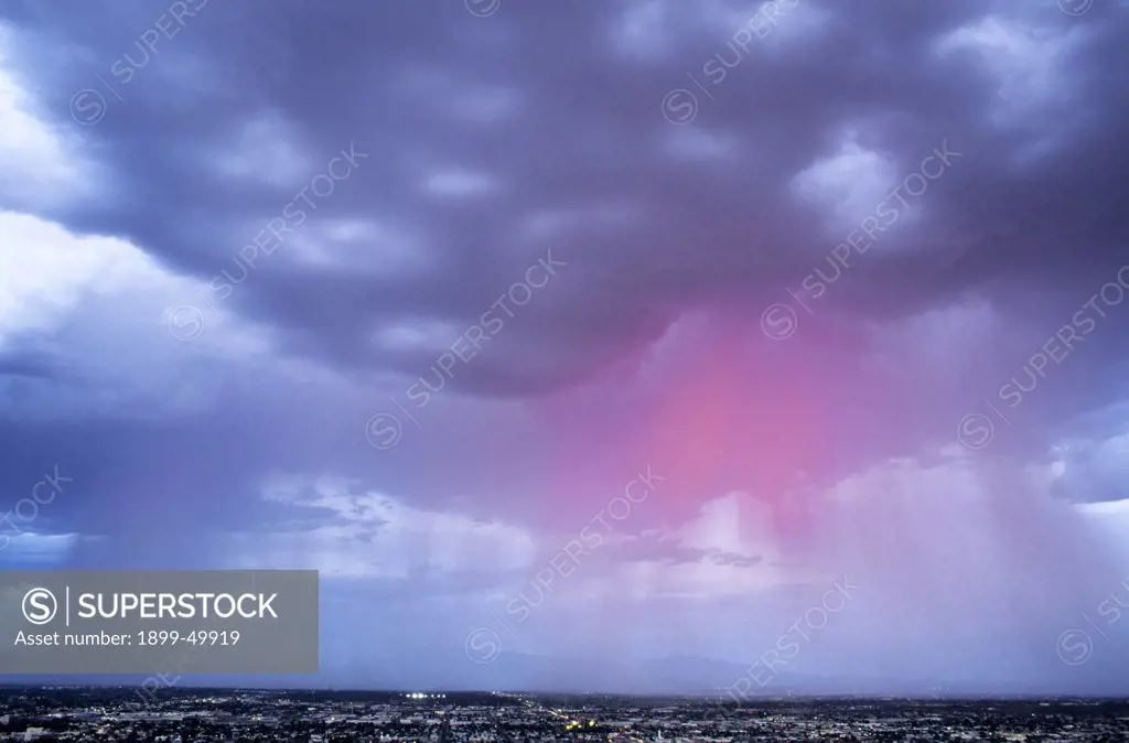 Shafts of pink rain at sunset beneath cumulonimbus clouds with mammatus formation in cloud base.  Cool air downdrafts form mammatus clouds. Sonoran Desert, Tucson, Arizona, USA.
