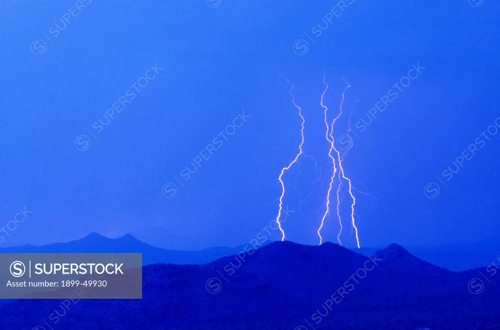 Four cloud-to-ground lightning discharges at twilight seen from the Tucson Mountains to the Roskruge Mountains on the horizon.  Southern Arizona, USA.