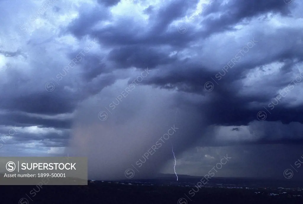 Afternoon rain storm, a cloudburst with cloud-to-ground lightning from leading edge of the rain shaft descending from a mature cumulonimbus cloud.  Tucson, Arizona, USA.