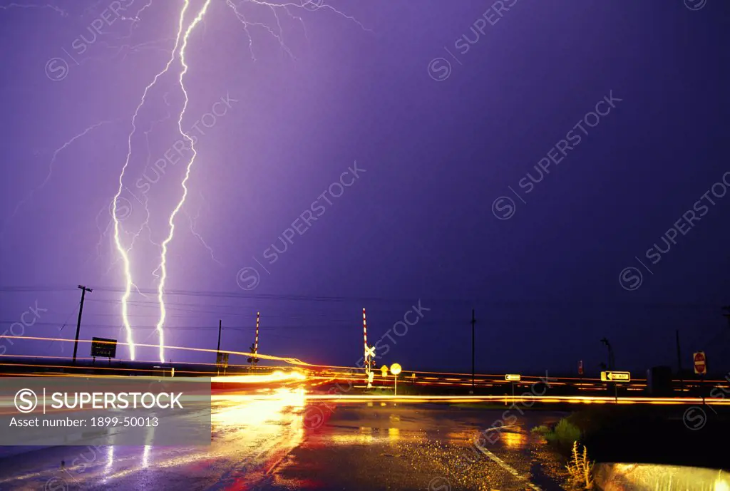 Car light trails and lightning with wet pavement and power lines near city street railroad crossing.  Tucson, Arizona, USA.