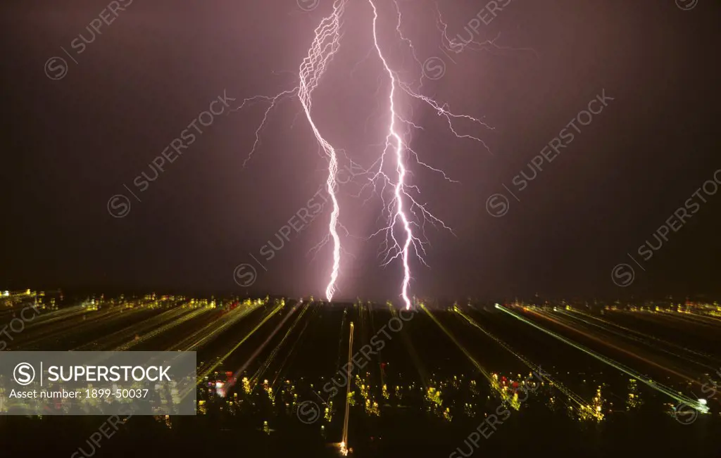 View of separated lightning strokes in a cloud-to-ground lightning strike over city at night, clearly visible in the upper portion of the flash on the left. This picture of scientific interest was made possible by zooming a photographic lens during the full interval of the lightning flash, thereby separating and recording on film each electrical stroke contained within the strike. The effect of zooming records the city lights as streaks across the film. Tucson, Arizona, USA.