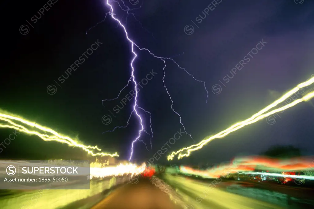 Nighttime storm on an interstate highway, with lightning strike and light trails from passing cars and trucks.   Tucson, Arizona, USA. Digitally altered sky/background