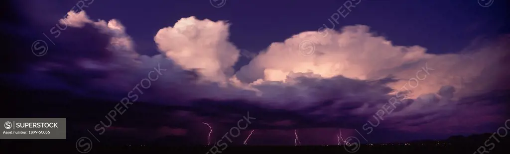 Swiftly moving storm cloud at sunset with cloud-to-ground lightning discharges from cloud base. Summer monsoon season, Sonoran Desert. South of Tucson, Arizona, USA. Panoramic 6x17 film