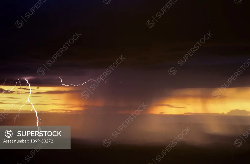 Overview of rain storm at sunset with rain curtains, cloud-to-ground lightning, and air discharge lightning.  Plains of San Agustin, New Mexico, USA.