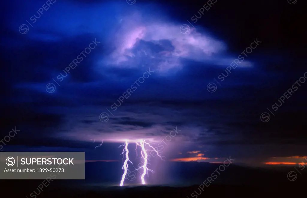 Overview of rain storm at sunset with rain curtains and cloud-to-ground lightning from a mature cumulonimbus cloud.   Plains of San Agustin, New Mexico, USA.