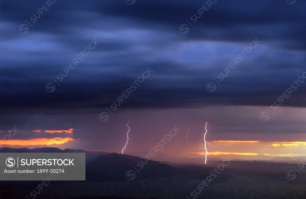 Overview of rain storm at sunset with rain curtains and cloud-to-ground lightning.  Plains of San Agustin, New Mexico, USA.