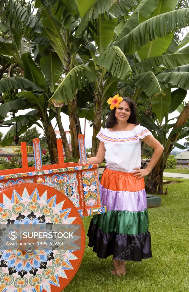 Costa Rican Woman In Traditional Dress Next To Traditional Carriage In And Around Costa Rica.