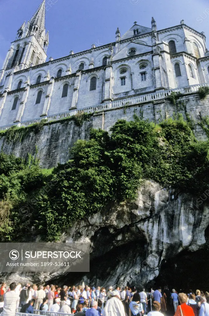 France. Lourdes.Church Above And Pilgrims Waiting To Enter The Grotto Of Miraculous Appearances Of Our Lady (Grotte Massabielle).