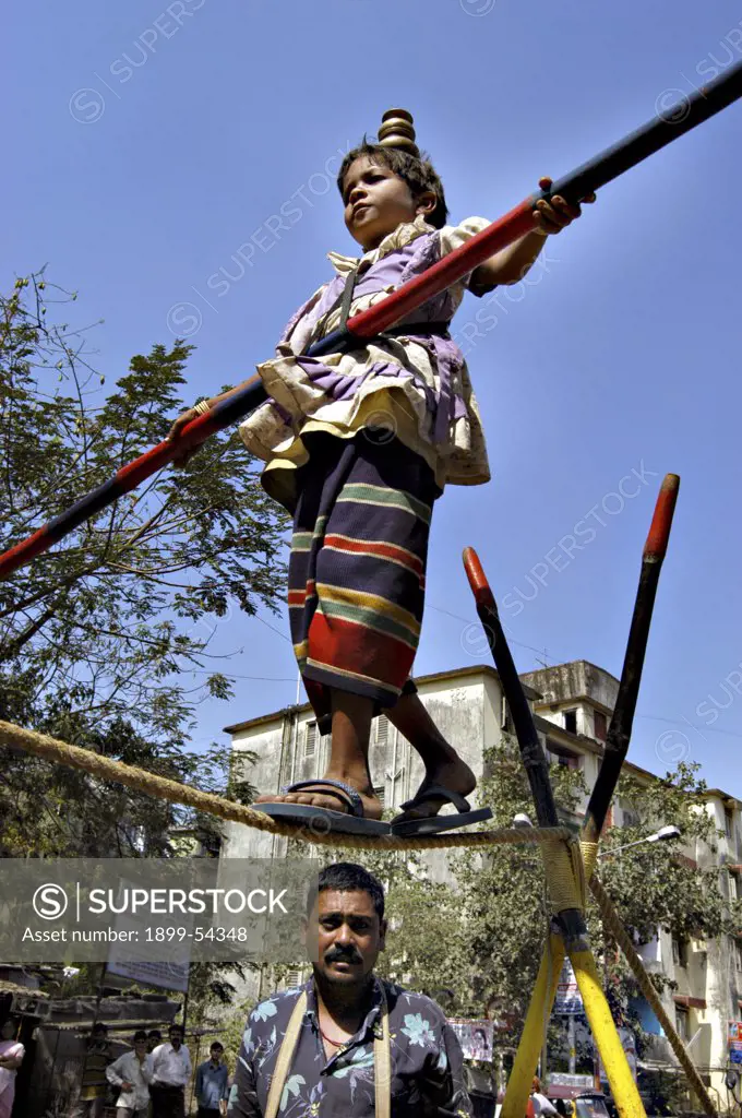 South Asian Girl Working Street Performer Balancing Act By Walking On Rope With Bamboo In Hand. Mumbai, India.
