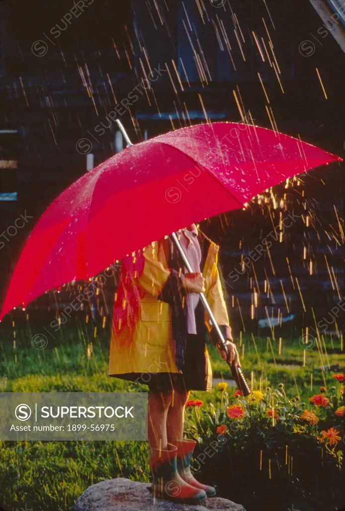 Young Child Under Red Umbrella (Face Hidden) In A Yellow Rain Slicker, Light Spring Shower