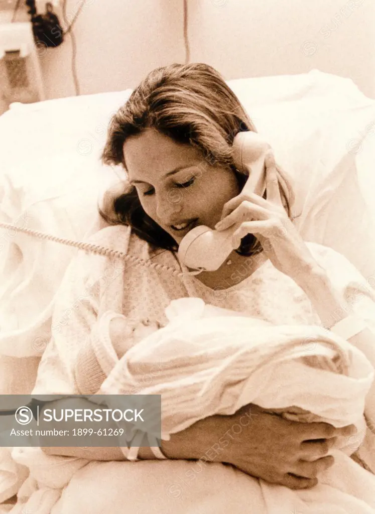 Mother In Hospital Bed, On Telephone, Holding Newborn Baby.