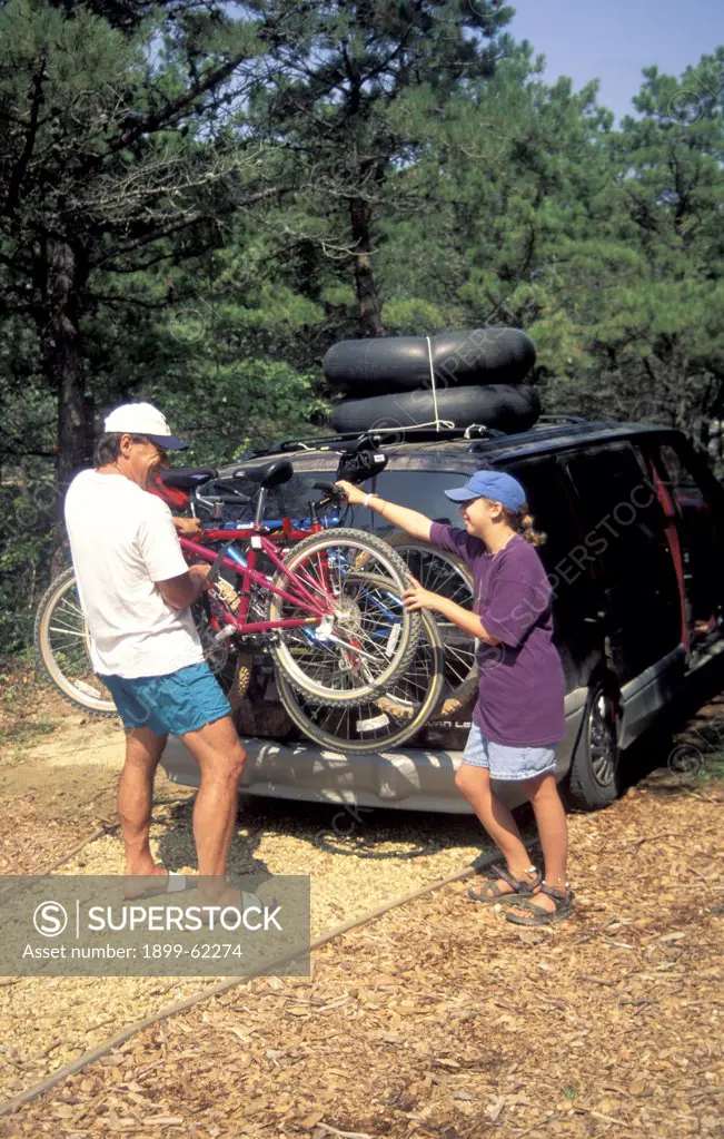 Father And Daughter Loading Minivan With Bikes And Inner Tubes