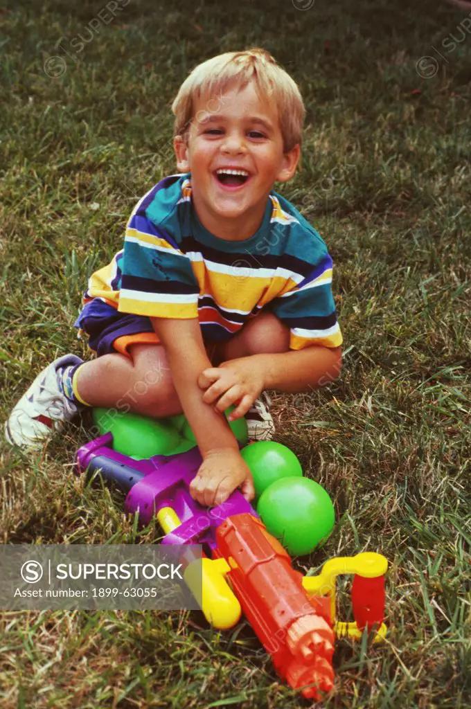 Five Year Old Blonde Little Boy With A Water Gun Smiling In A Backyard