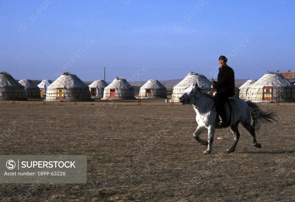 China, Inner Mongolia. Mongolian Rider On Horse.Yurts (Traditional Housing) In Background