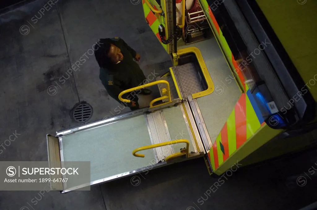 UK, London, ambulance technician unloading wheelchair ramp of ambulance