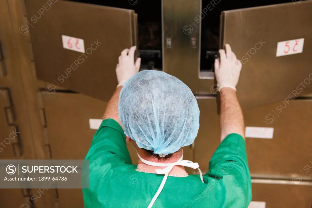 Mortuary technician opening doors to mortuary refrigerator