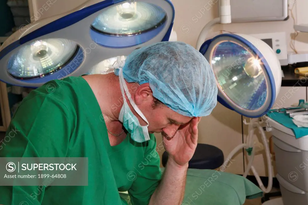 Stressed surgeon holding head in hand