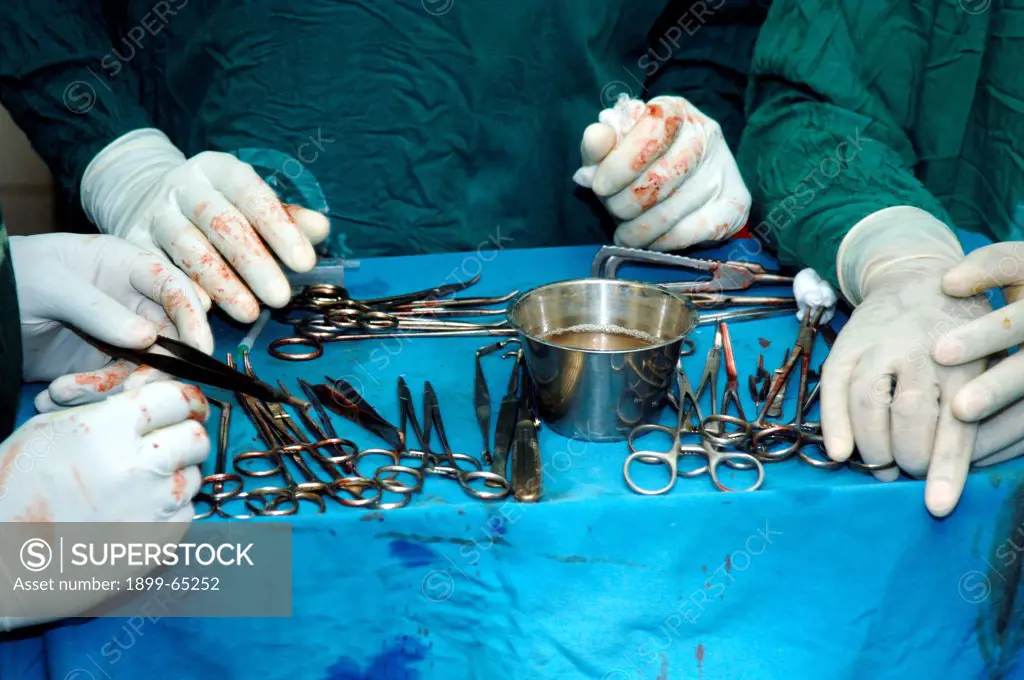 Blood stained gloved hands gather tray of surgical equipment