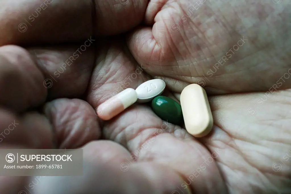 Assortment of medication tablets on elderly man's hand