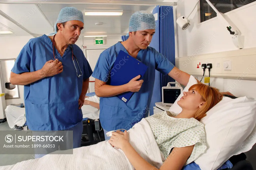 Two doctors, wearing blue surgical gowns and caps, consulting with patient in hospital