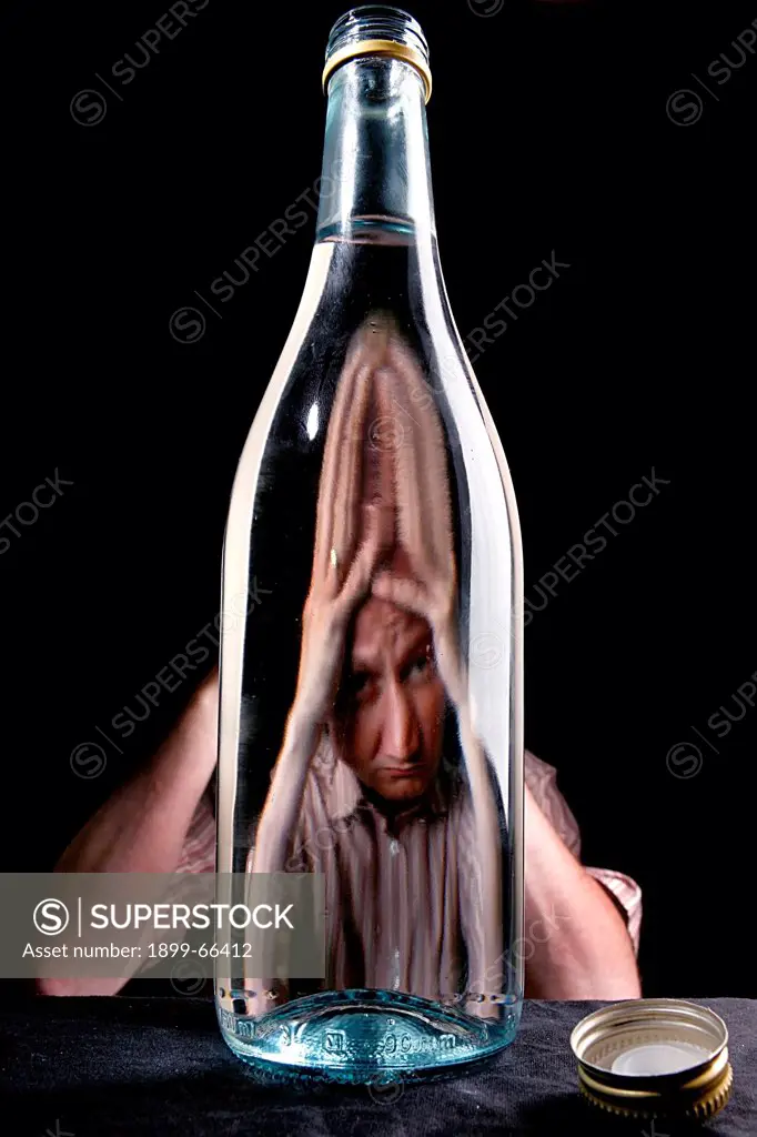 Distorted face of man through empty bottle of alcohol