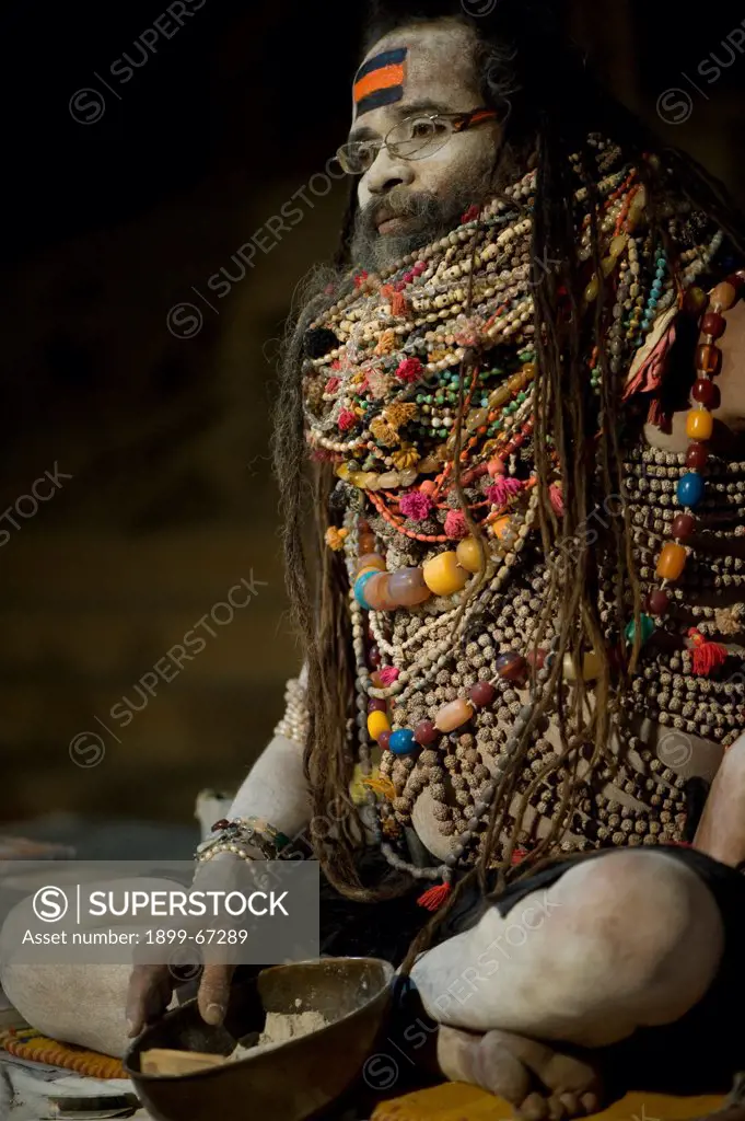 Lali Baba, a priest in Varanasi, waiting for worshipers that he will bless with ash (in the bowl at his feet). He is wearing necklaces given to him to worship Shiva.