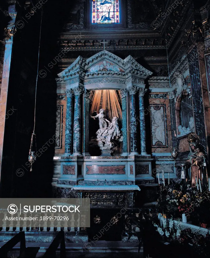 Italy, Lazio, Rome, Church of Santa Maria della Vittoria. Whole artwork view. Axial view of the sculptural group with the angel striking the body of St. Teresa with an arrow, under the gilted rays coming from the top of the baroque aedicula, convex towards the aisle.