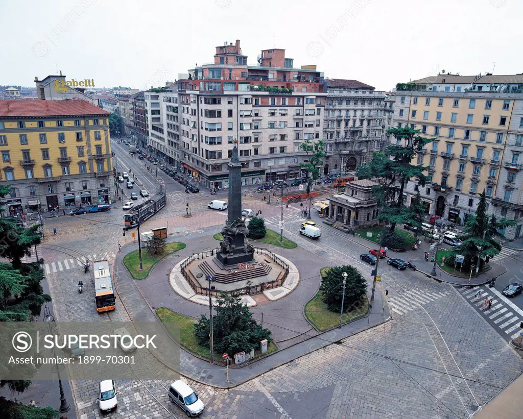 Italy, Lombardy, Milan, Piazza Cinque Giornate. View from above of the square, with the obelisk bearing the war memorial monument in the centre. It is made of five women statues, each one representing one of the five days of battle. Four grass borders are at the four corners, the streets are around the monument and some buildings surround the square.