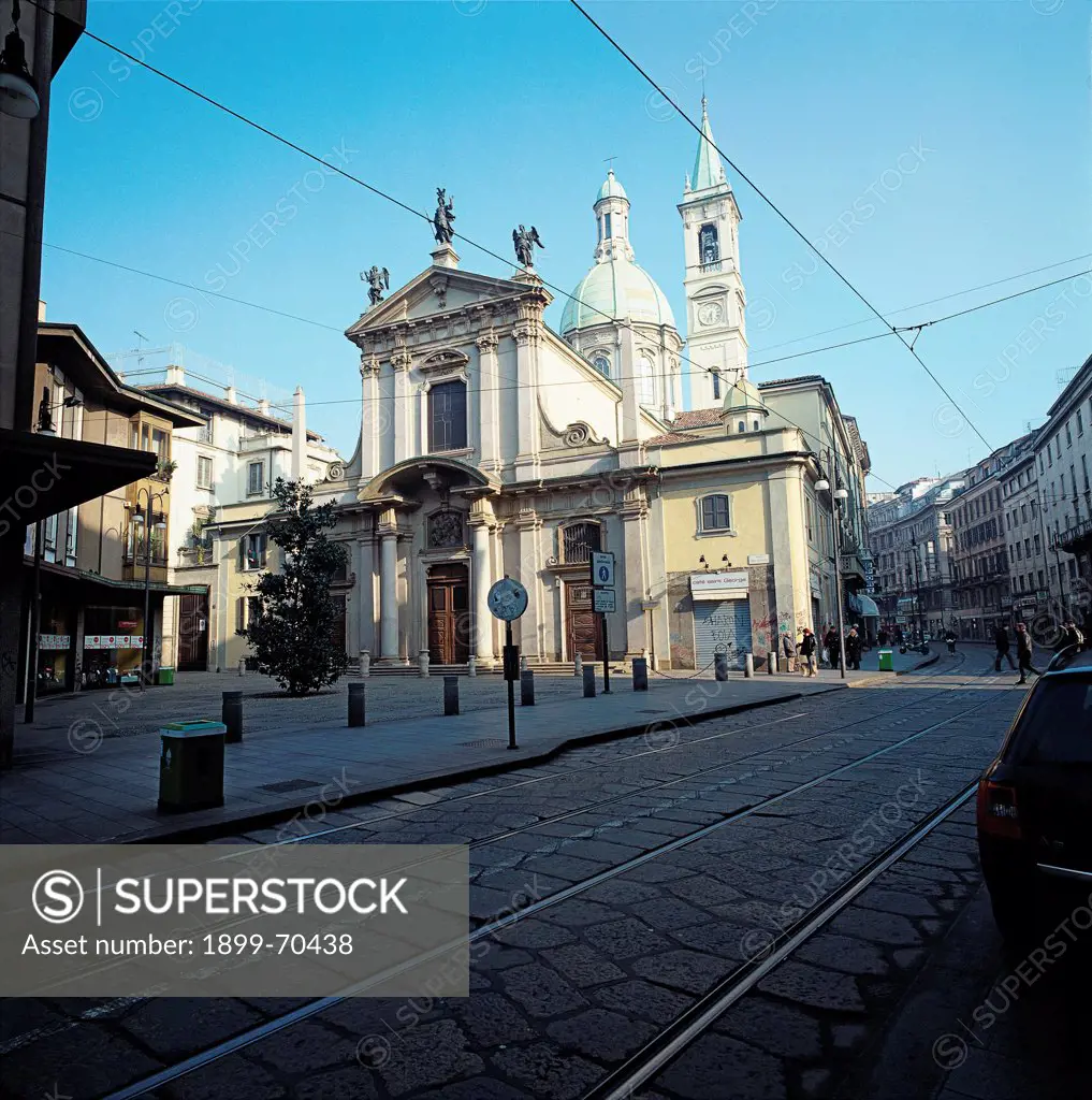 Italy, Lombardy, Milan. Whole artwork view. Foreshortening of the square and the facade of the church, that presents pediment, tympanum, portal, bell tower, columns, lesenes, statues and a dome.