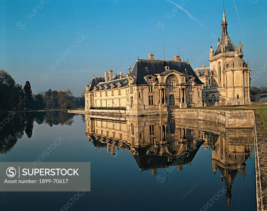France, Chantilly, Chateau de Chantilly. Whole artwork view. The shape of the castle reflects itself in a pond.