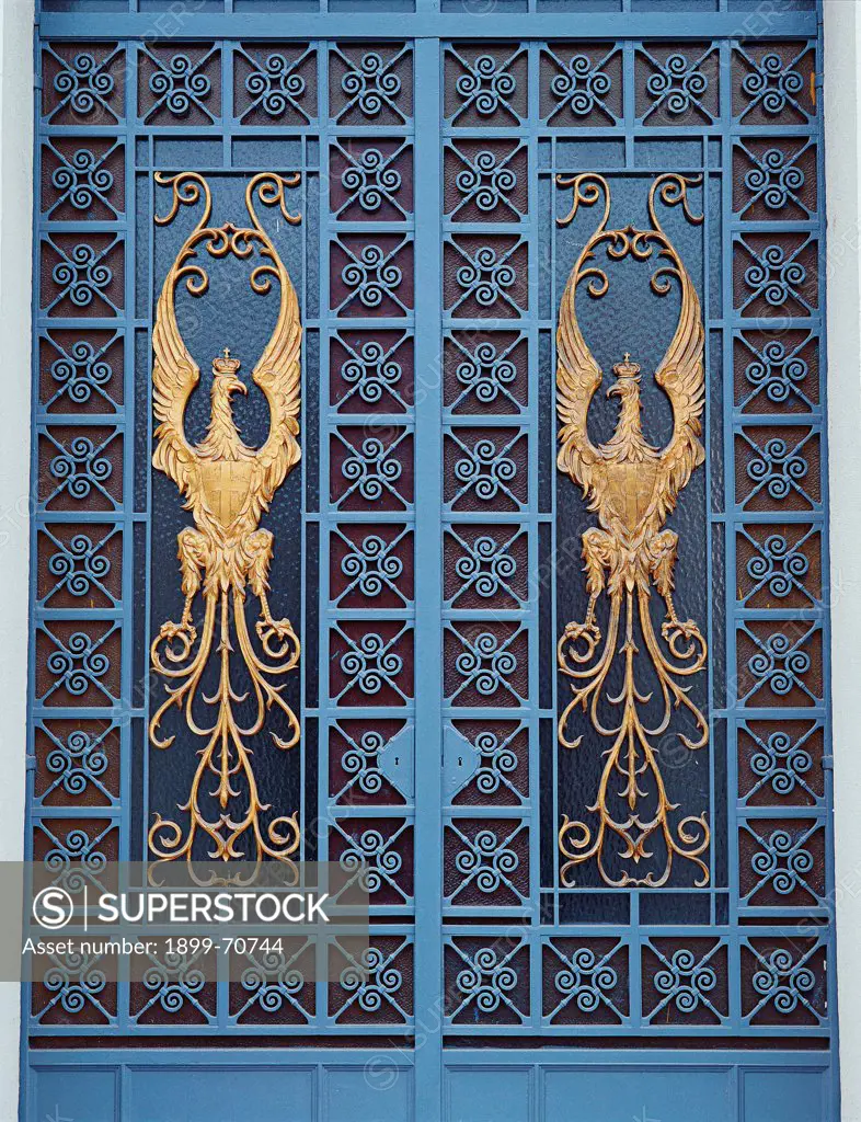 Italy, Calabria, Reggio Calabria, Prefecture Palace. Detail. A detail of wrought iron decoration of a door. In the middle a golden eagle and all around a blue geometric decoration.
