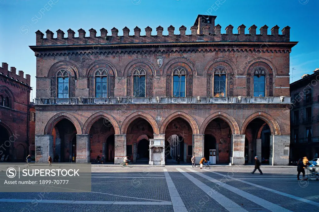 Italy, Lombardy, Cremona, Municipal Building. Whole artwork view. The facade of the town hall seen from the square in front of it. The building has on the ground floor an ogival-arched porch and it is crowned with battlements.