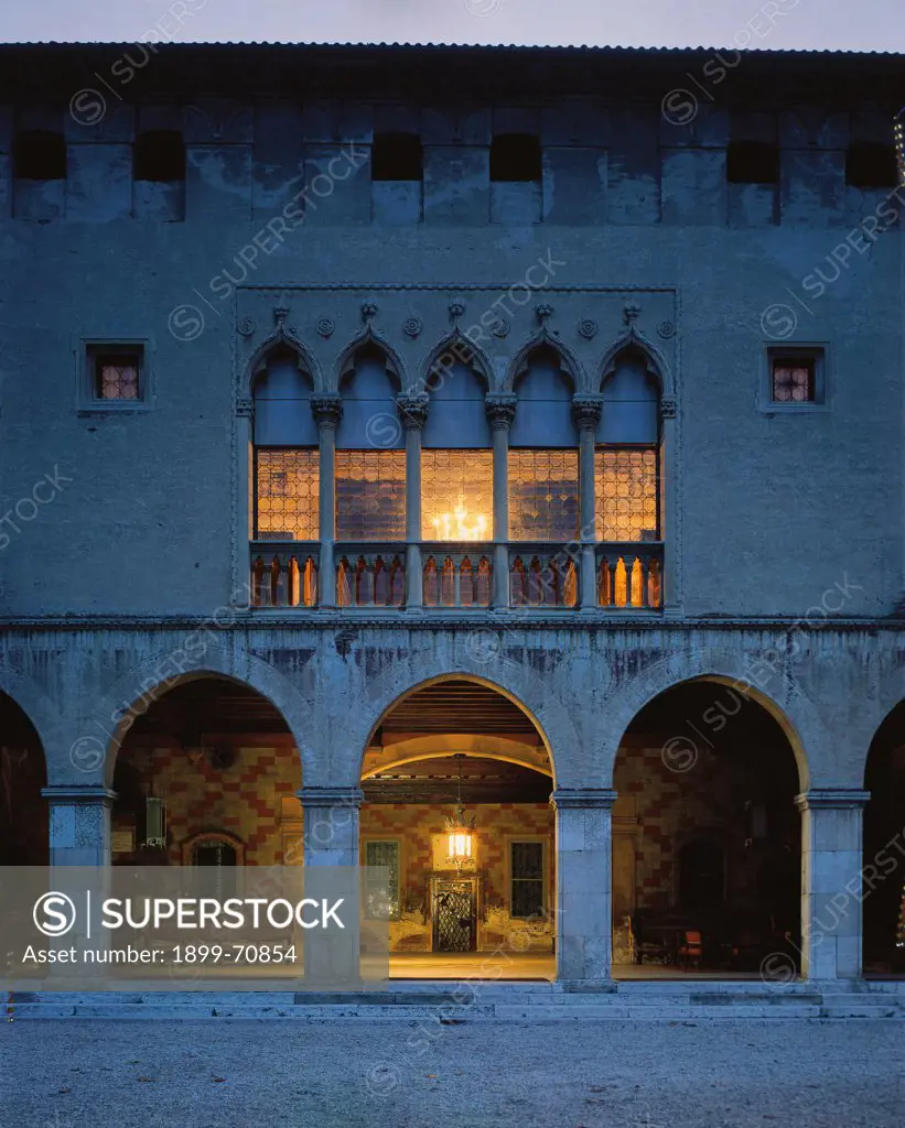 Italy, Veneto, Thiene, Porto Colleoni Castle. Night view of the facade with a Gothic five-lancet window and a portico with round arches. On the top, Ghibellines battlements (walled today).