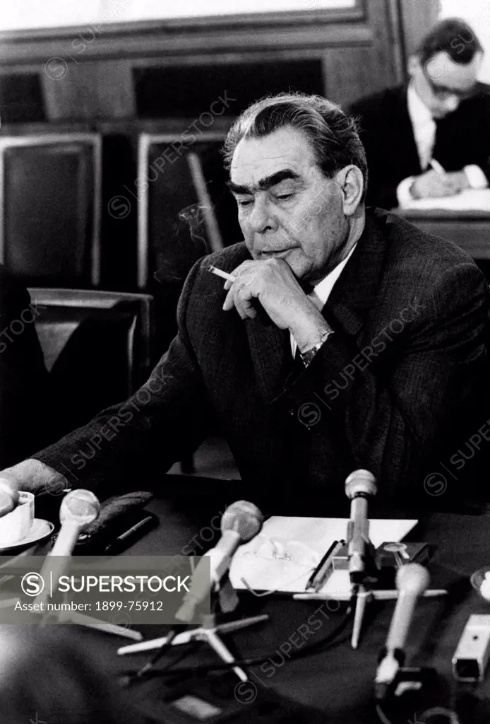 General Secretary of the Central Committee of the Communist Party of the Soviet Union, Leonid Ilyich Brezhnev, smokes a cigarette during a press conference, with the desk full of many microphones and a cup of tea. Moscow (Soviet Union), June 1973.