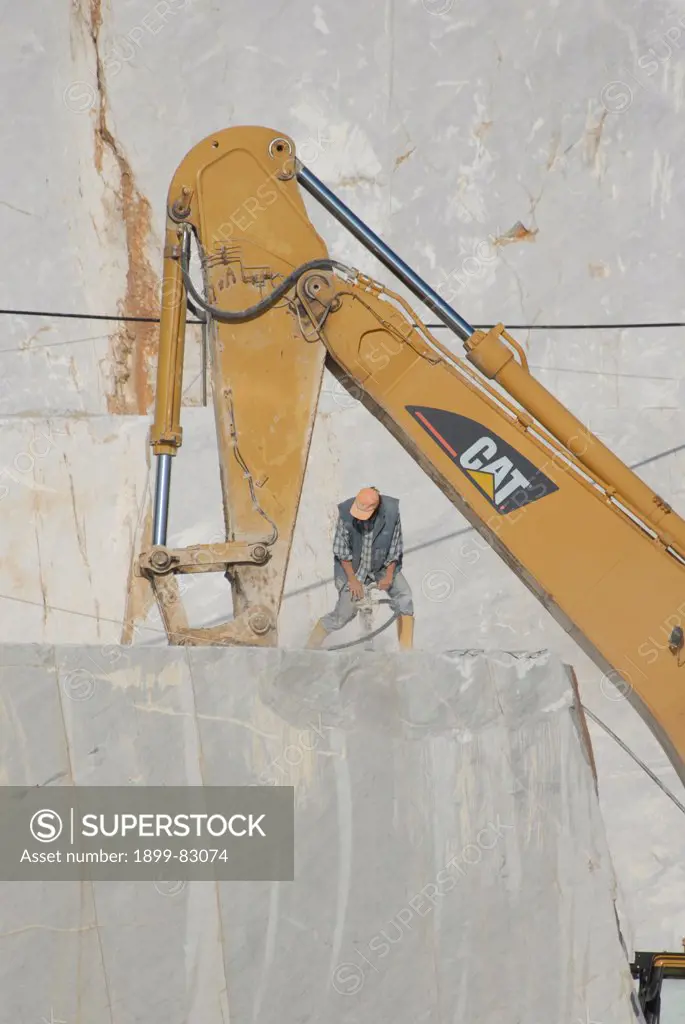 Man drilling a hole to start a new cut near an excavator