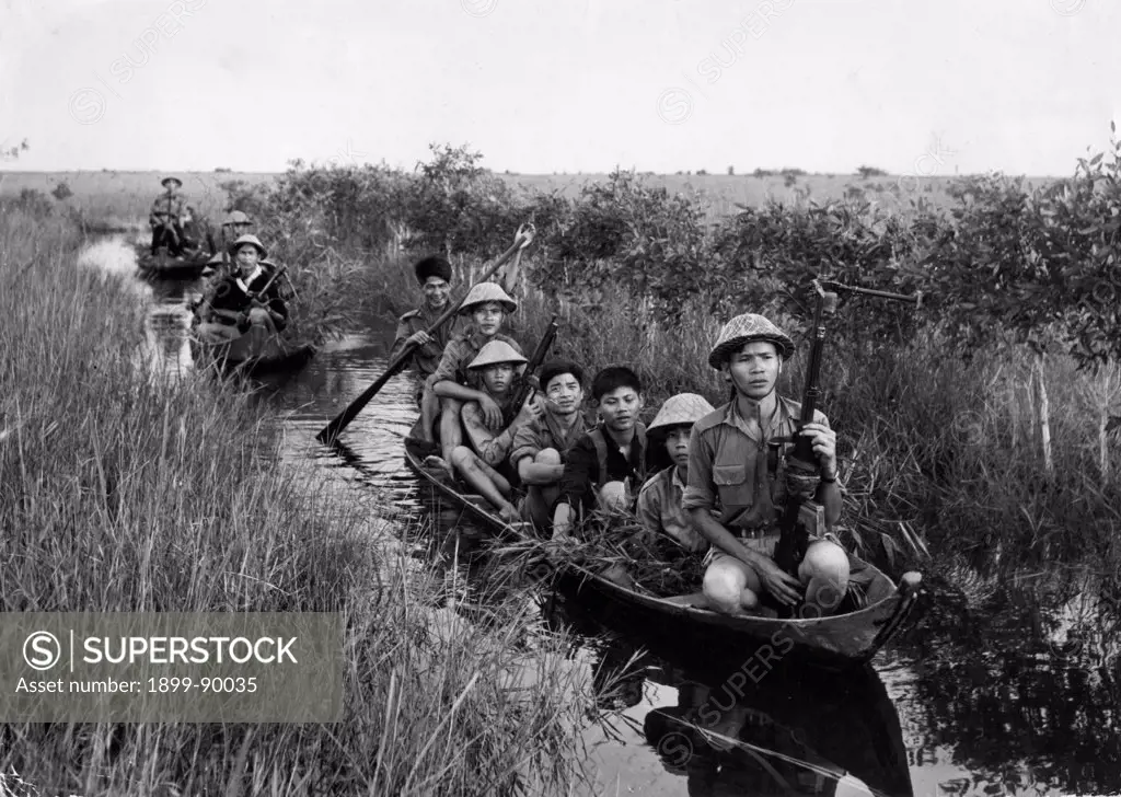 Communist guerrillas (Viet Cong) travel in small boats through a swamp under cover of reeds on thir way to making a surprise attack on US forces in Dong Thap Muoi area, South Vietnam. Vietnam War. 1966.